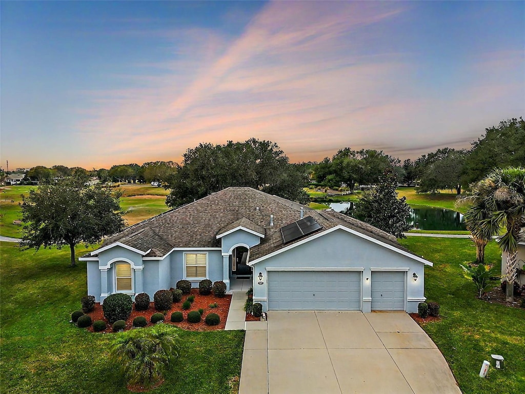 ranch-style home featuring a garage, a water view, a yard, and solar panels