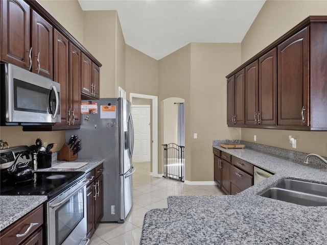 kitchen featuring stainless steel appliances, light stone countertops, dark brown cabinetry, sink, and light tile patterned flooring