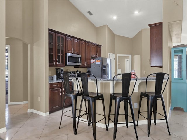 kitchen with light stone counters, light tile patterned flooring, dark brown cabinetry, a breakfast bar, and appliances with stainless steel finishes