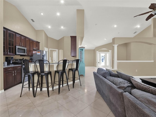 kitchen with vaulted ceiling, stainless steel appliances, decorative columns, a breakfast bar area, and dark brown cabinetry