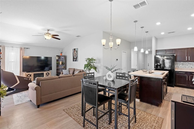 dining space featuring ceiling fan with notable chandelier, light hardwood / wood-style flooring, vaulted ceiling, and sink