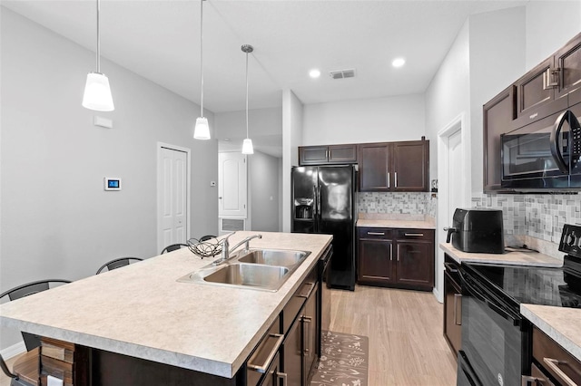 kitchen featuring decorative backsplash, a kitchen island with sink, sink, black appliances, and pendant lighting