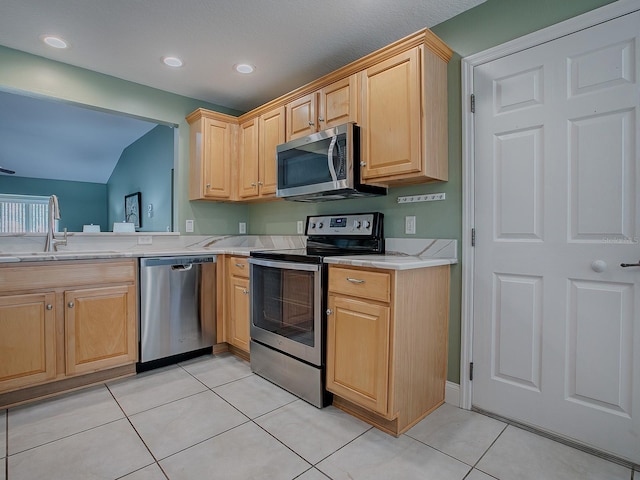 kitchen with vaulted ceiling, sink, light tile patterned flooring, appliances with stainless steel finishes, and light brown cabinetry