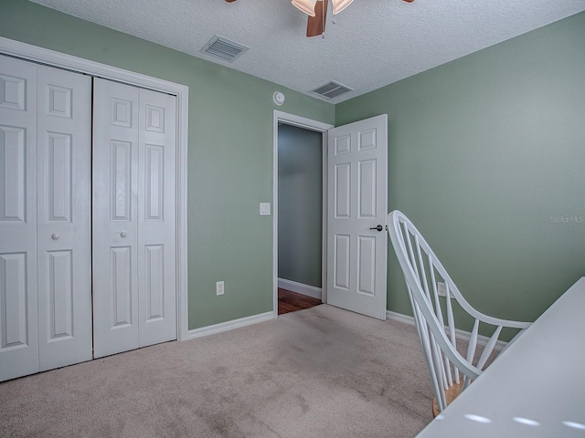 unfurnished bedroom featuring ceiling fan, a textured ceiling, a closet, and light carpet