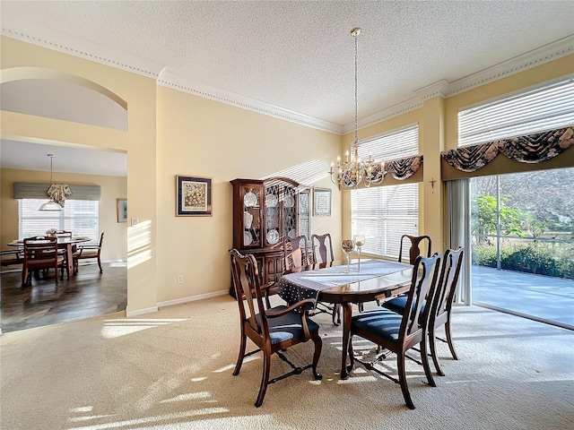 carpeted dining space featuring a healthy amount of sunlight, a textured ceiling, crown molding, and a notable chandelier