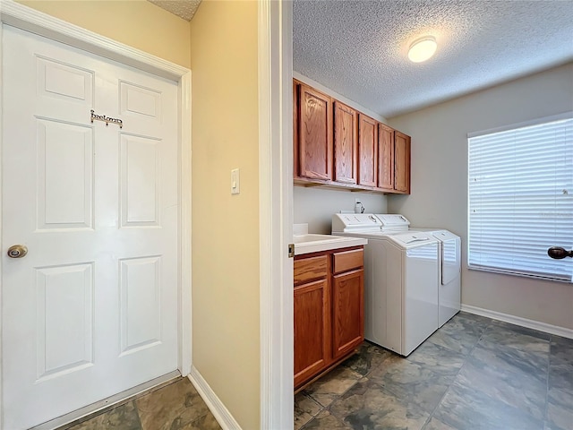 laundry room featuring washing machine and clothes dryer, cabinets, and a textured ceiling