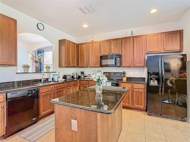 kitchen featuring light tile patterned flooring, dark stone counters, black appliances, sink, and a kitchen island