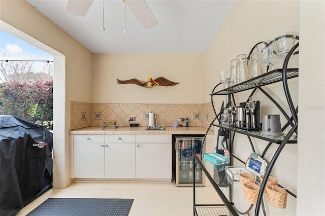 kitchen with ceiling fan, wine cooler, white cabinets, and tasteful backsplash