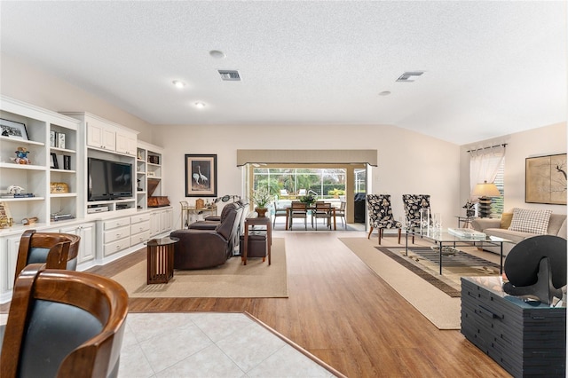 living room featuring vaulted ceiling, a textured ceiling, and light hardwood / wood-style floors