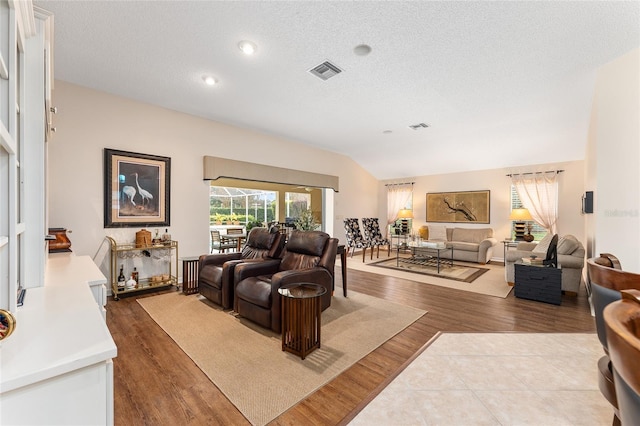 living room with light wood-type flooring, a textured ceiling, and vaulted ceiling