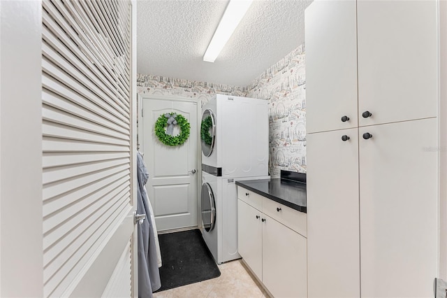 laundry room with cabinets, a textured ceiling, stacked washer / drying machine, and light tile patterned flooring