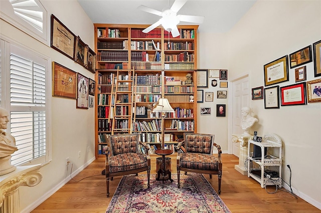 living area with light wood-style floors, bookshelves, baseboards, and a ceiling fan