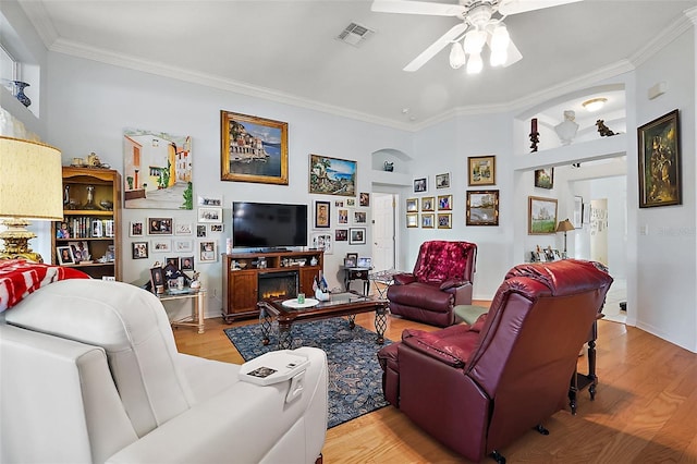 living room featuring a warm lit fireplace, visible vents, wood finished floors, and ornamental molding