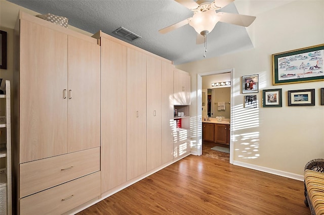 unfurnished bedroom with visible vents, light wood-style flooring, connected bathroom, a textured ceiling, and baseboards