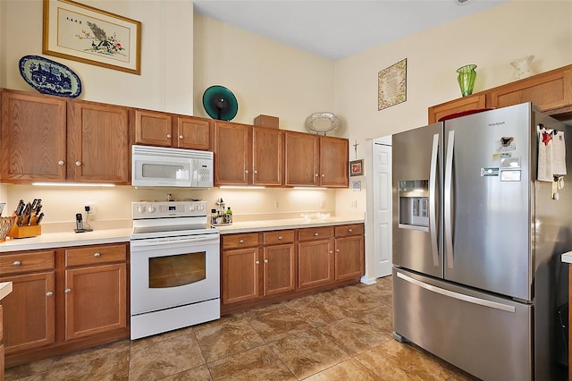 kitchen with a towering ceiling, white appliances, brown cabinetry, and light countertops