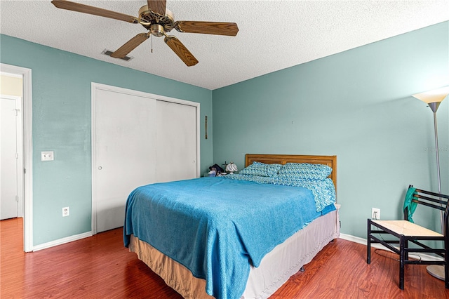 bedroom with dark wood-type flooring, a textured ceiling, ceiling fan, and a closet