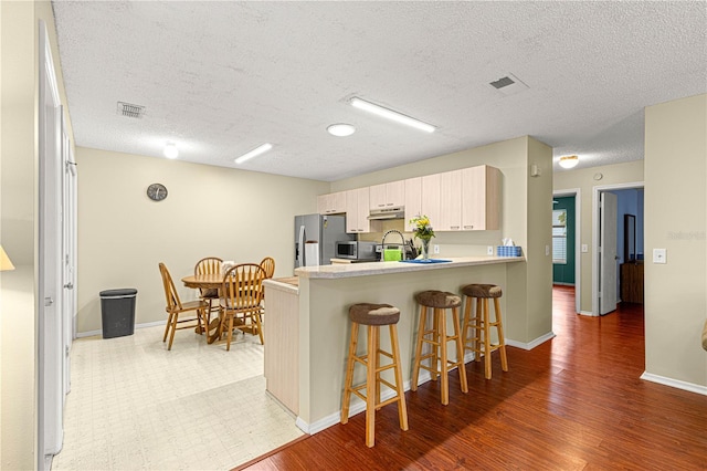 kitchen featuring stainless steel appliances, a textured ceiling, a kitchen bar, kitchen peninsula, and dark wood-type flooring