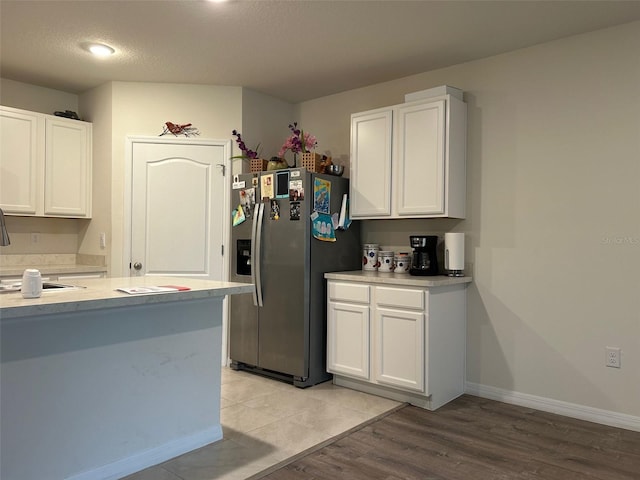 kitchen with white cabinets, sink, stainless steel refrigerator with ice dispenser, light wood-type flooring, and a textured ceiling