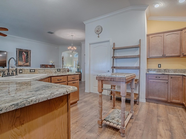 kitchen with sink, crown molding, light stone counters, hanging light fixtures, and light hardwood / wood-style floors