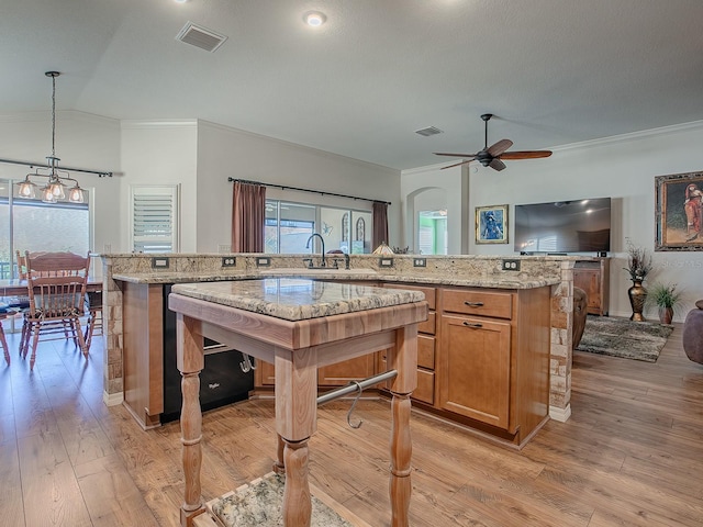 kitchen with light stone counters, decorative light fixtures, light wood-type flooring, ornamental molding, and ceiling fan