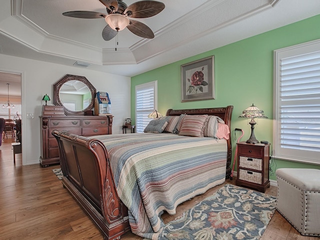 bedroom with crown molding, ceiling fan, wood-type flooring, and a raised ceiling