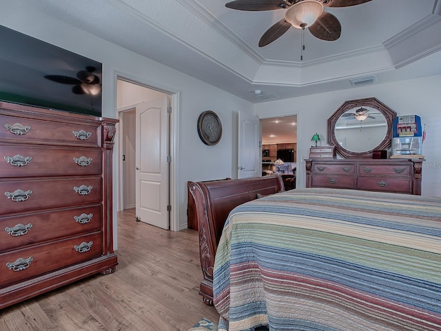 bedroom featuring crown molding, a tray ceiling, ceiling fan, and light wood-type flooring