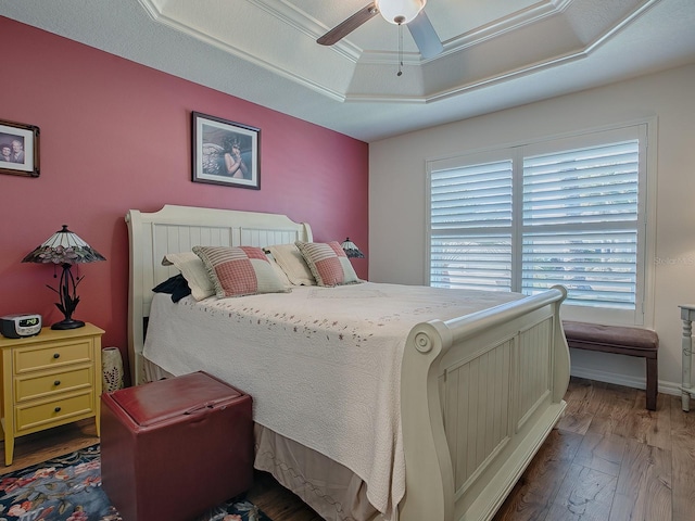 bedroom featuring dark wood-type flooring, ceiling fan, a raised ceiling, and multiple windows