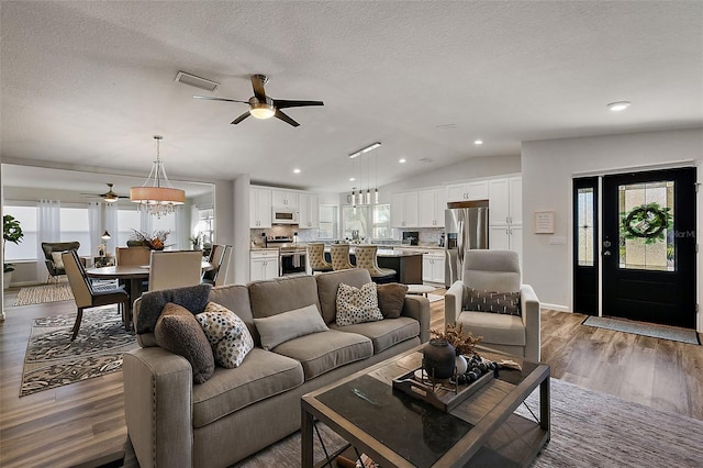 living room with ceiling fan with notable chandelier, a textured ceiling, vaulted ceiling, and hardwood / wood-style floors