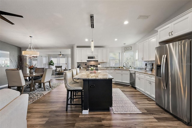 kitchen with decorative light fixtures, appliances with stainless steel finishes, white cabinetry, and a center island