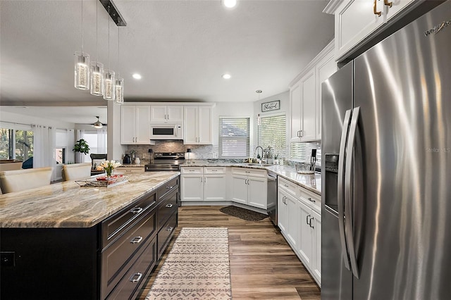 kitchen featuring appliances with stainless steel finishes, a center island, sink, white cabinetry, and decorative light fixtures