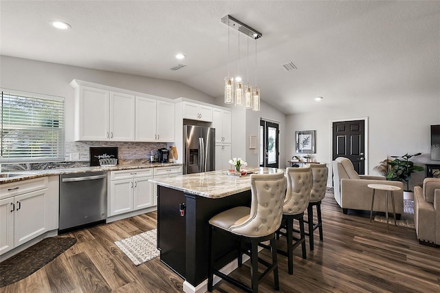 kitchen with decorative light fixtures, stainless steel appliances, decorative backsplash, a kitchen island, and white cabinetry