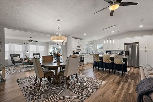 dining room with a textured ceiling, lofted ceiling, ceiling fan with notable chandelier, rail lighting, and dark wood-type flooring