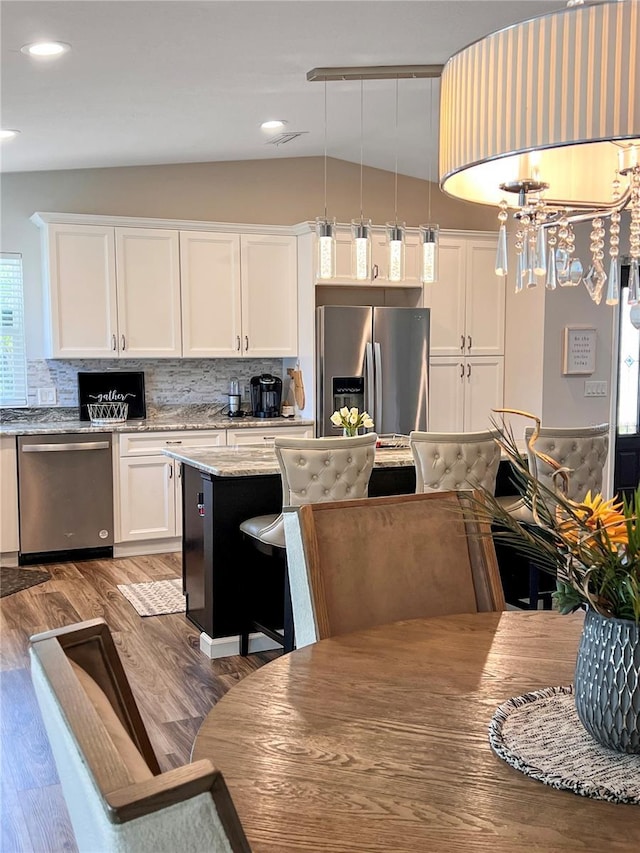 kitchen with light stone countertops, hanging light fixtures, white cabinets, appliances with stainless steel finishes, and wood-type flooring