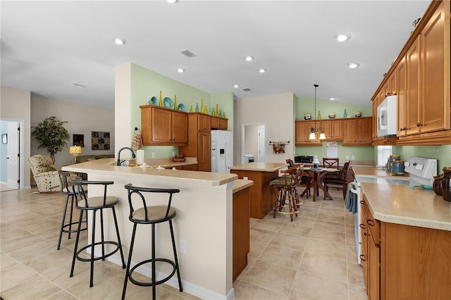 kitchen featuring decorative light fixtures, vaulted ceiling, white appliances, a kitchen bar, and kitchen peninsula