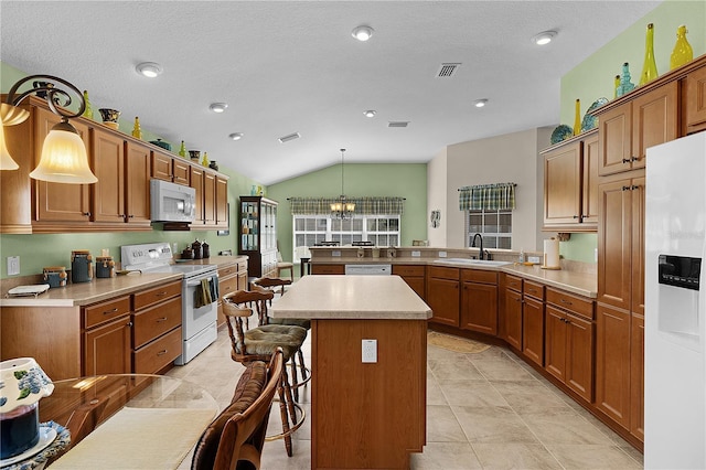 kitchen featuring white appliances, kitchen peninsula, pendant lighting, lofted ceiling, and sink