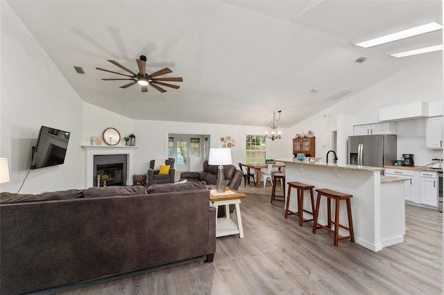 living room with ceiling fan with notable chandelier, light wood-type flooring, lofted ceiling, and sink