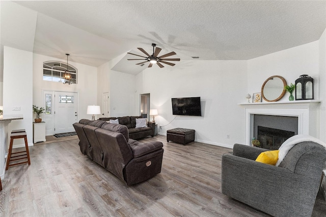 living room featuring hardwood / wood-style floors, ceiling fan with notable chandelier, a textured ceiling, and vaulted ceiling