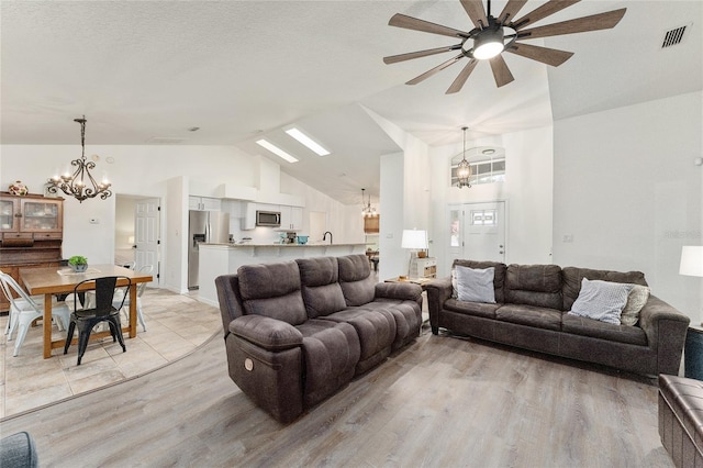 living room featuring ceiling fan with notable chandelier, light hardwood / wood-style floors, a textured ceiling, and vaulted ceiling