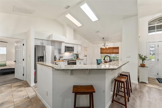 kitchen featuring a chandelier, stainless steel appliances, light stone counters, and a breakfast bar area