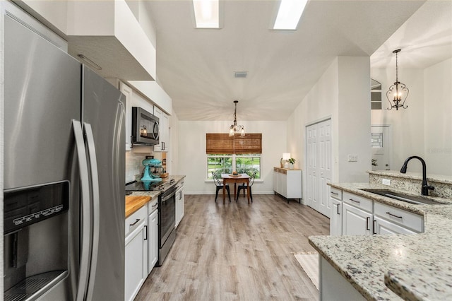 kitchen with stainless steel appliances, sink, white cabinets, a chandelier, and hanging light fixtures