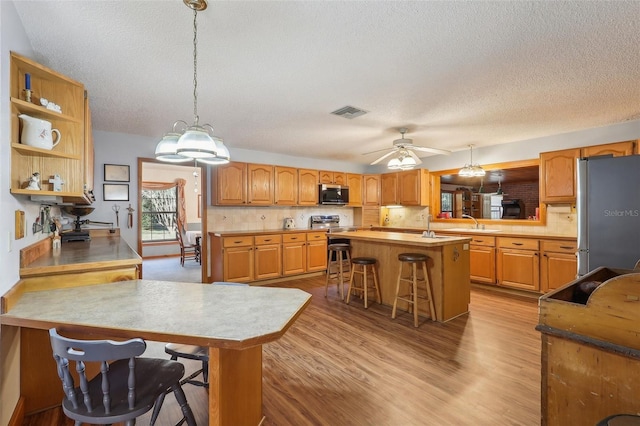 kitchen featuring stainless steel appliances, kitchen peninsula, decorative light fixtures, a breakfast bar area, and a kitchen island