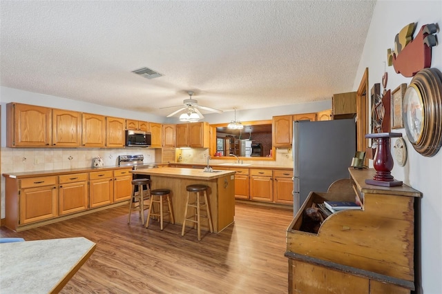 kitchen featuring sink, appliances with stainless steel finishes, a kitchen bar, a kitchen island, and light wood-type flooring