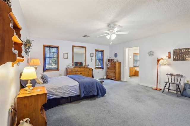 bedroom with a textured ceiling, connected bathroom, light colored carpet, and ceiling fan