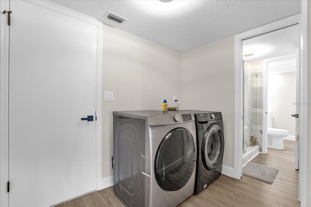 washroom with washing machine and dryer, light hardwood / wood-style flooring, and a textured ceiling