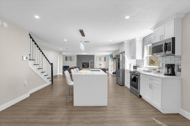 kitchen with white cabinetry, wood-type flooring, a kitchen island with sink, and appliances with stainless steel finishes