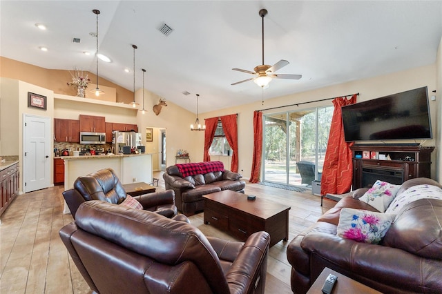 living room with ceiling fan with notable chandelier, high vaulted ceiling, and light wood-type flooring