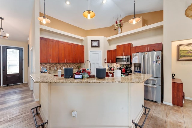 kitchen with kitchen peninsula, a breakfast bar area, stainless steel appliances, decorative backsplash, and hanging light fixtures