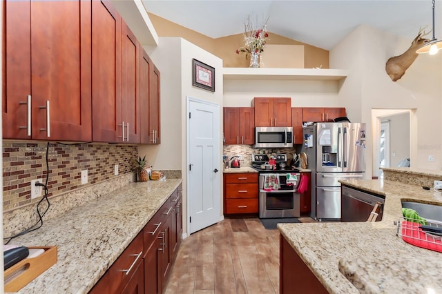 kitchen with appliances with stainless steel finishes, decorative backsplash, high vaulted ceiling, light stone counters, and light hardwood / wood-style flooring