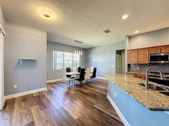 kitchen with dark hardwood / wood-style flooring, decorative light fixtures, sink, tasteful backsplash, and light stone counters