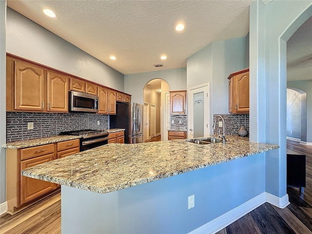 kitchen featuring appliances with stainless steel finishes, sink, light stone countertops, and kitchen peninsula